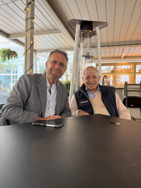 Bob Leaf, smiling, seated at an outdoor café table beside a friend.